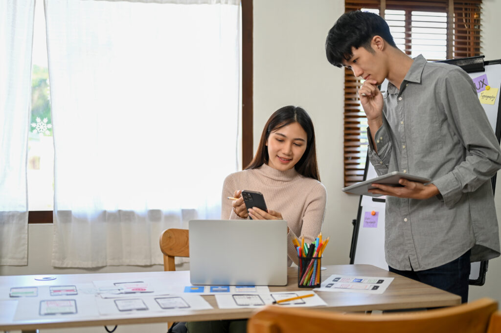 Professional millennial Asian male and female developers are in the meeting room, working together on their new mobile application prototype. UI UX business startup concept